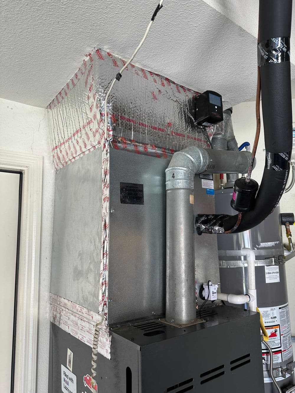 Furnace installation in garage with insulated ductwork and water heater nearby.