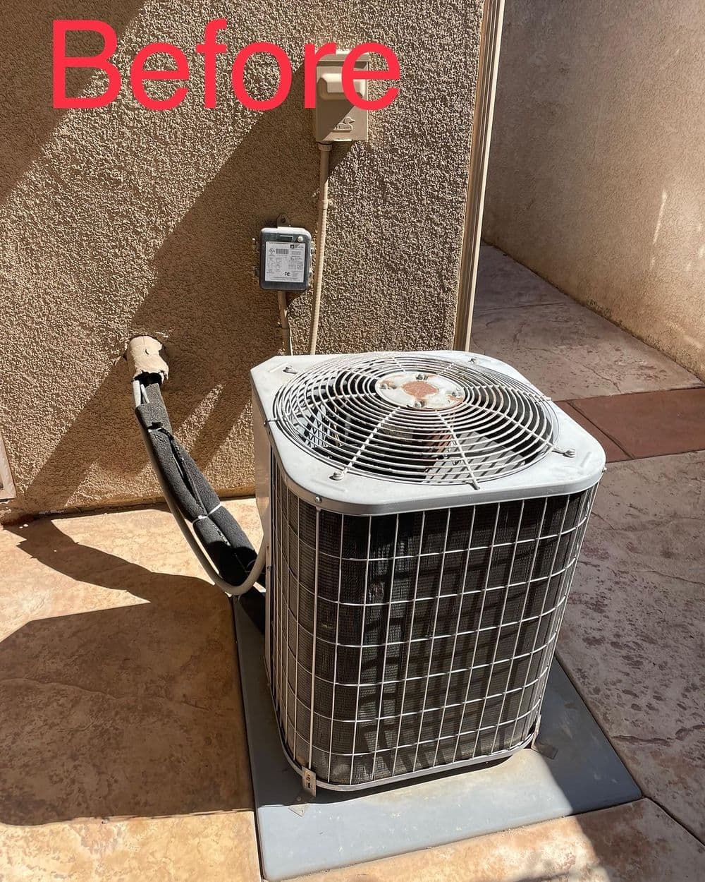 Old air conditioning unit in need of repair, installed on a stone patio with electrical connections.