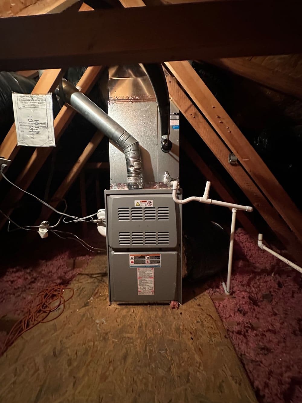 Attic furnace installation with ductwork and insulation visible in a dimly lit space.