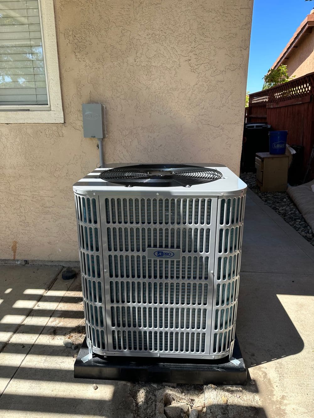 Air conditioning unit installed beside wall, with sunlight casting shadows on pavement.