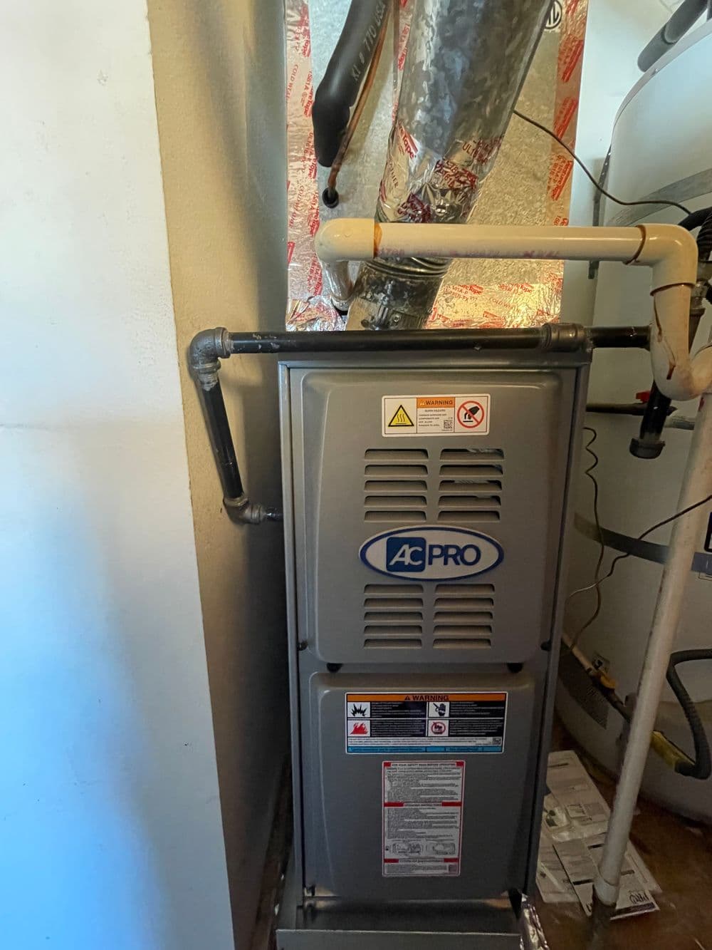 AC Pro furnace installation in a residential utility room with safety labels and ductwork.