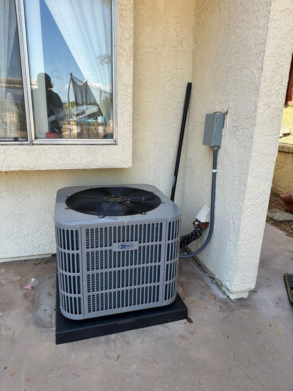 Air conditioning unit outside a house next to a window, showcasing residential cooling system.