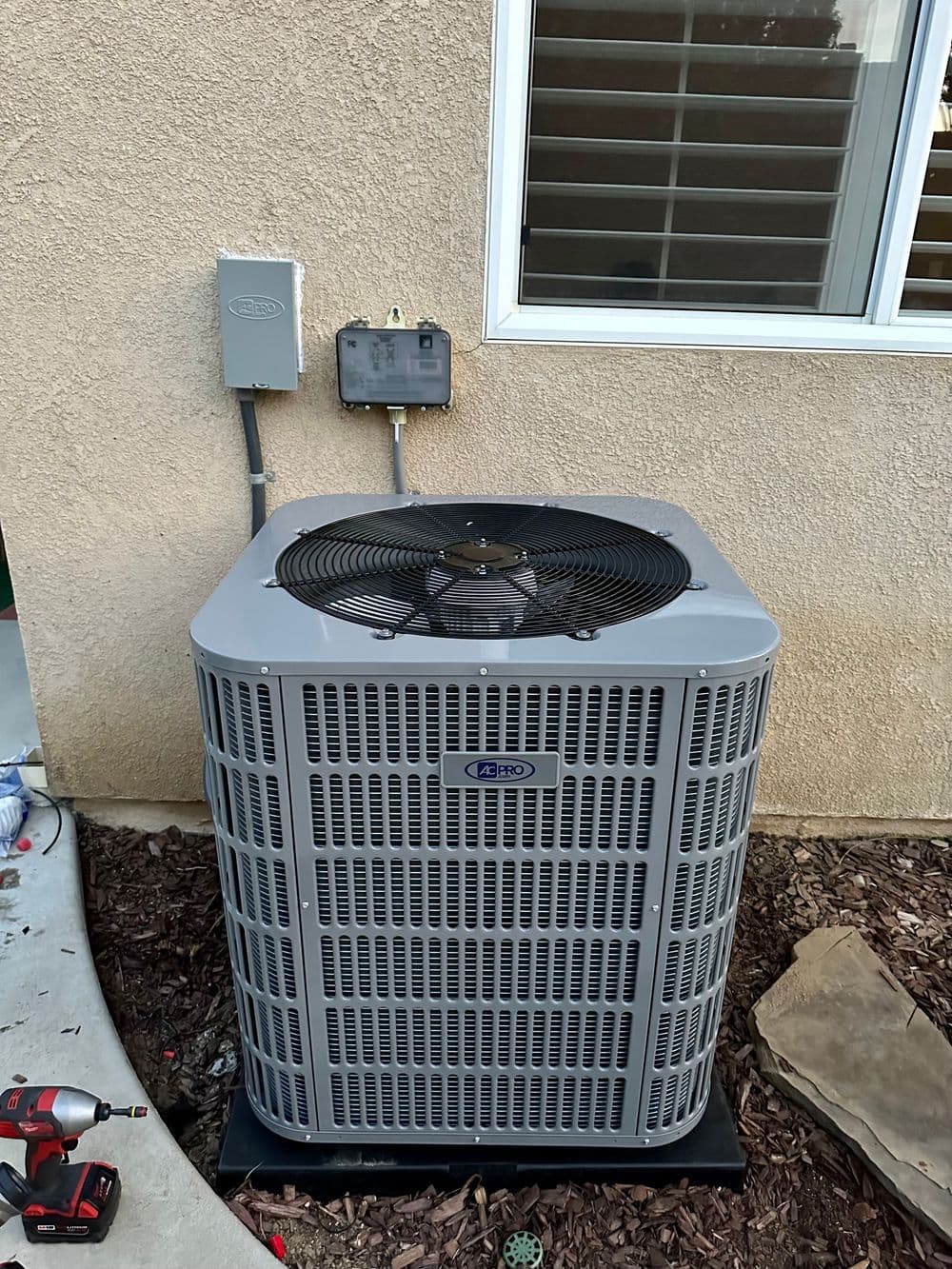 Air conditioning unit installed outside a home with a power connection and tools nearby.